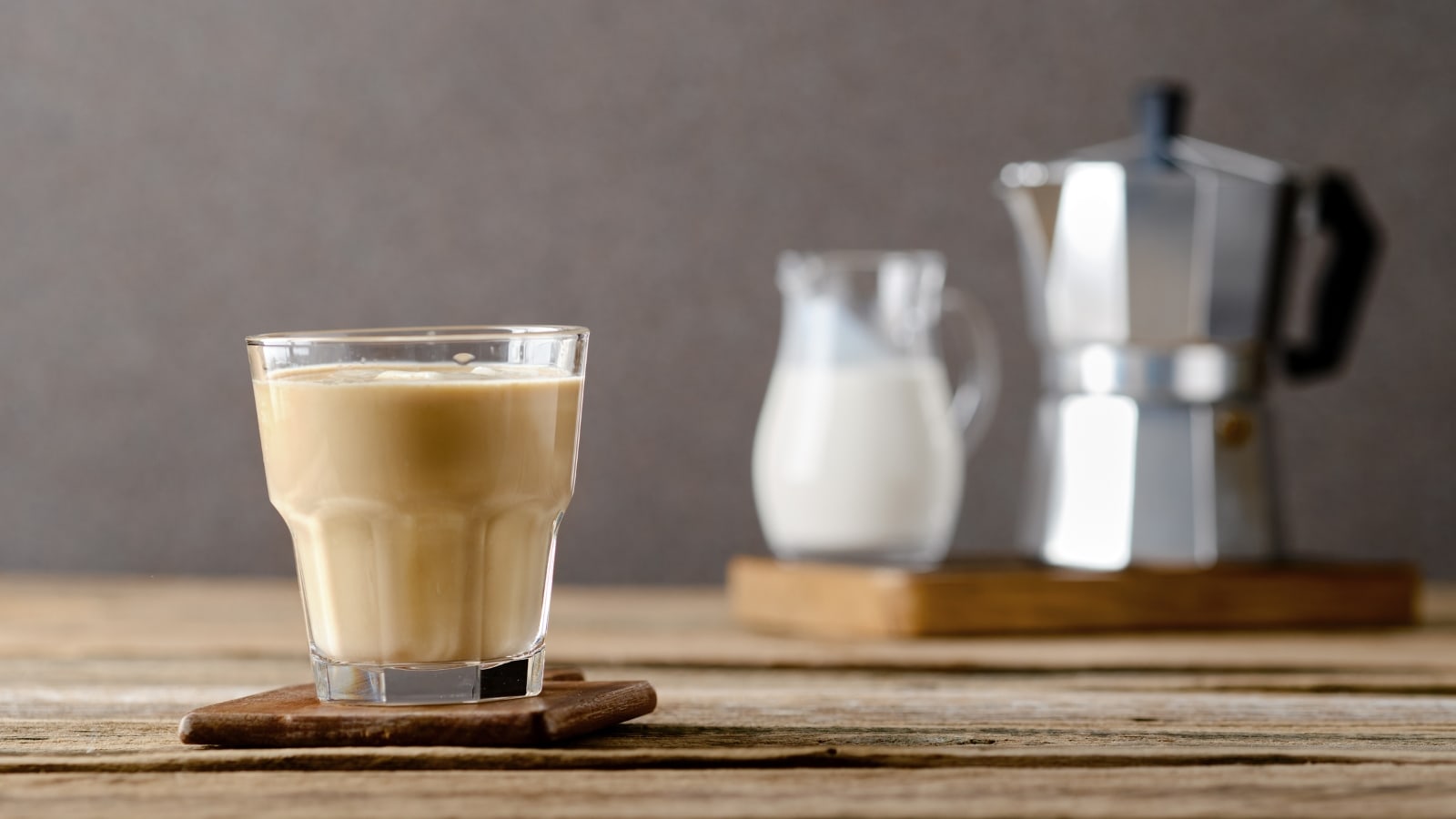 a glass of No-Foam Latte against the blurred Italian Coffee Pot and jug of milk