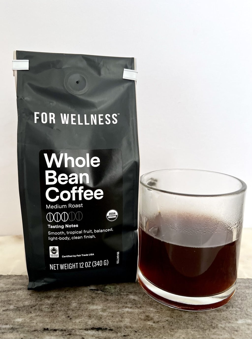 A pack of For Wellness Whole Bean Coffee Medium Roast Coffee stands next to a brewed cup of coffee 