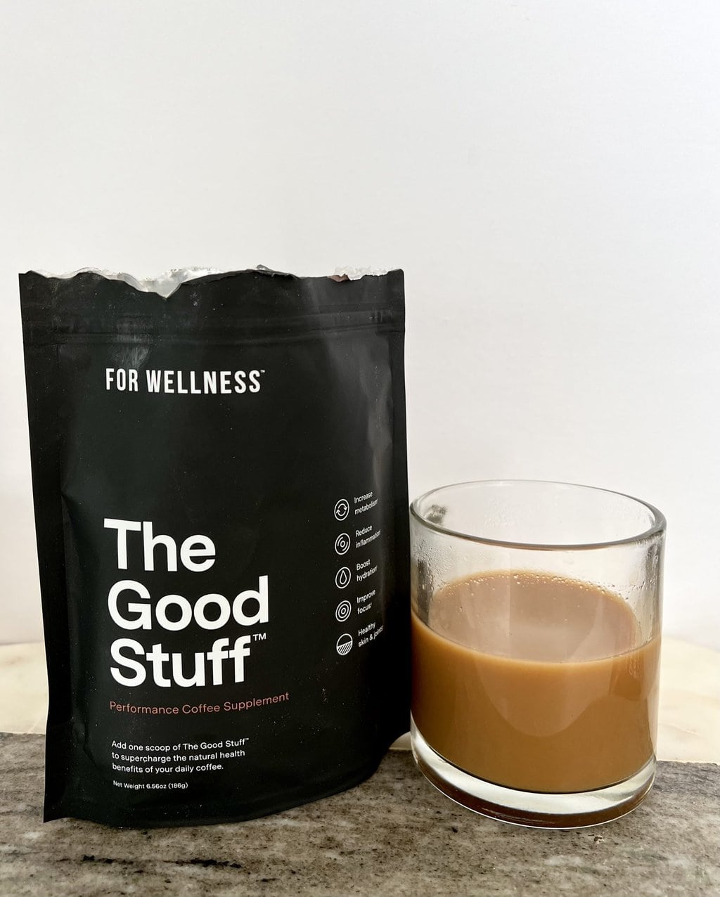 For Wellness The Good Stuff package of coffee additives stands next to a brewed cup of liquid